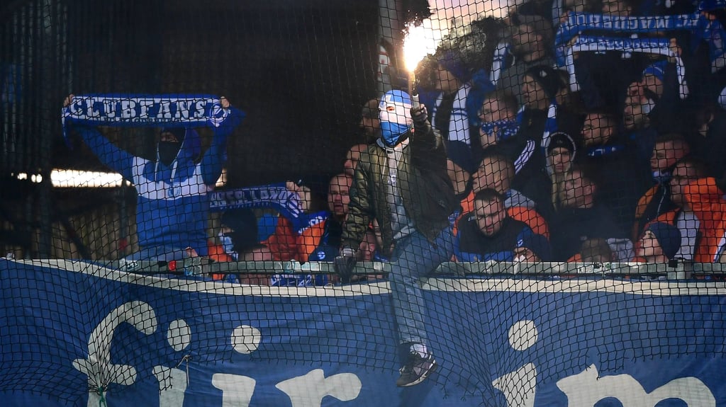 Ein vermummter Fan des 1. FC Magdeburg brennt beim DFB-Pokal-Spiel bei Holstein Kiel eine bengalische Fackel ab.