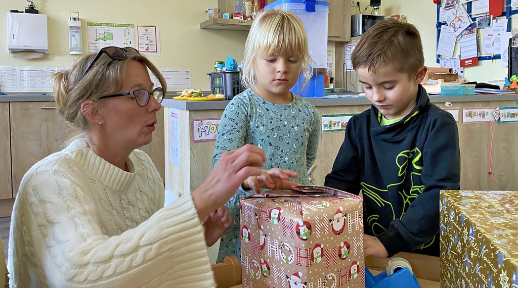 Pauline und Leon packen gemeinsam mit Erzieherin Kerstin Bohne Pakete für den Weihnachtspäckchenkonvoi, der diese dann zu bedürftigen Kindern nach Osteuropa bringt.