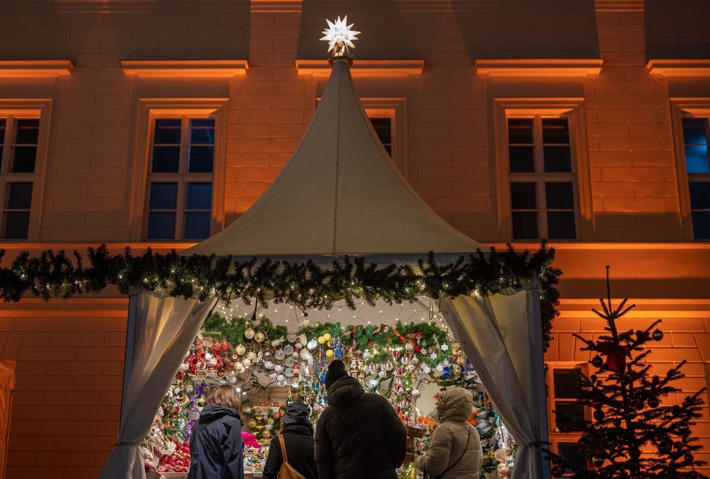Besucher eines Weihnachtsmarktes stehen an einem Verkaufsstand für Christbaumschmuck.
