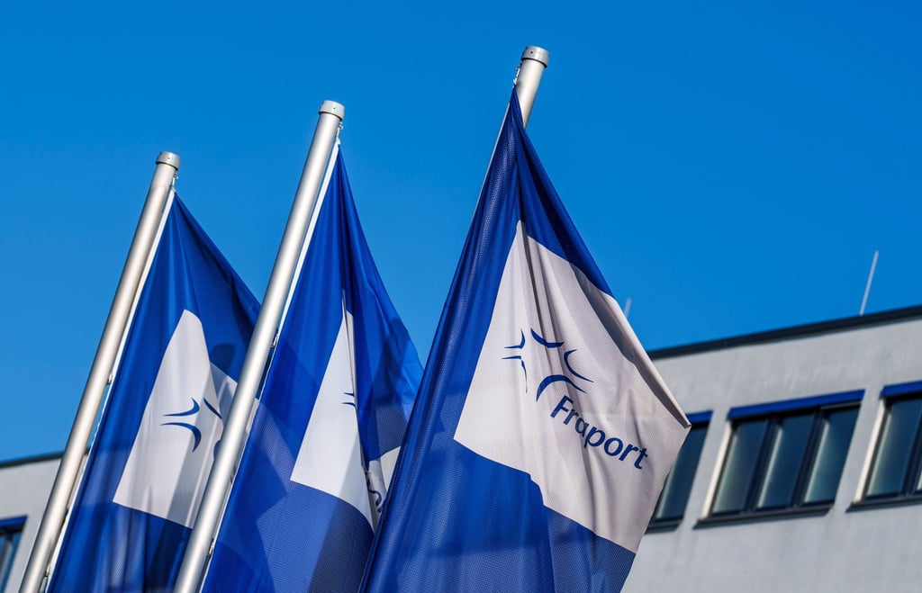 Flaggen mit dem Logo der Fraport AG wehen vor der Firmenzentrale im Wind.