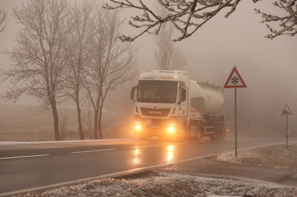 Ein Lkw fährt bei Glatteis und Nebel über eine Straße.