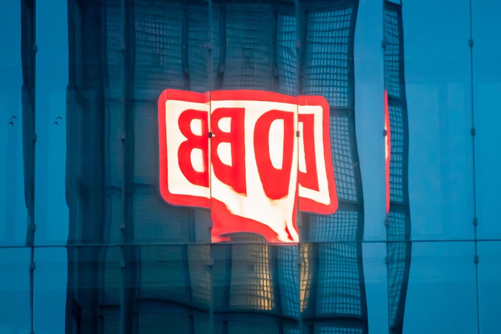 Das Logo der Deutschen Bahn AG (DB) am Berliner Hauptbahnhof spiegelt sich am Morgen in einer Gebäudefassade.