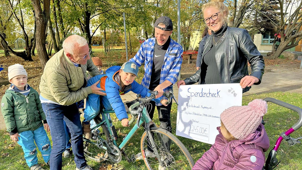 Luca darf sich auf das Rennrad setzen. Hans-Dieter Dammering hält ihn fest, während Ultracycler Andy Hesse das Rad erklärt.
