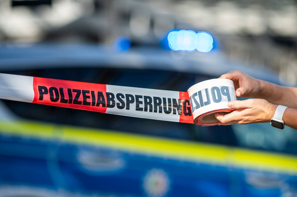 Ein Absperrband wird vor einem Polizeiwagen ausgerollt.