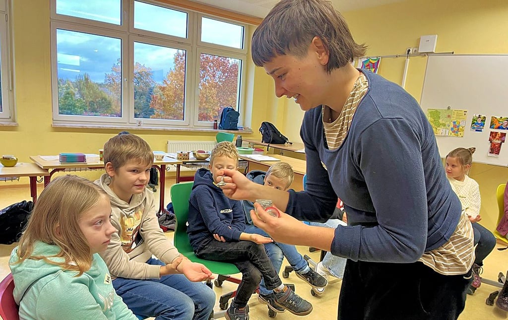 Charlotte Bast vom Verein „Carpus“ ließ die Kinder der 4b die Komponenten von Schokolade probieren. Sie teilt kleine Kakaobutterdrops aus.