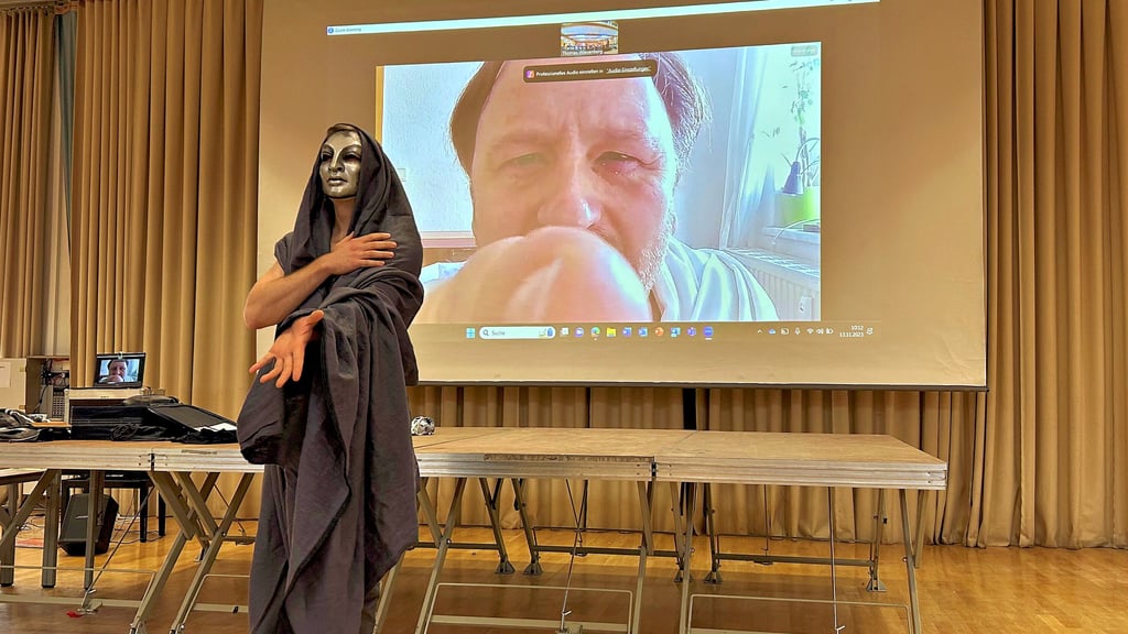 Thomas Wiesenberg als Antigone im Vordergrund in der Aula des Magdeburger Norbertusgymnasiums. Tobias Hübsch als verschlafener Kollege, der per Zoom zugeschaltet wird.