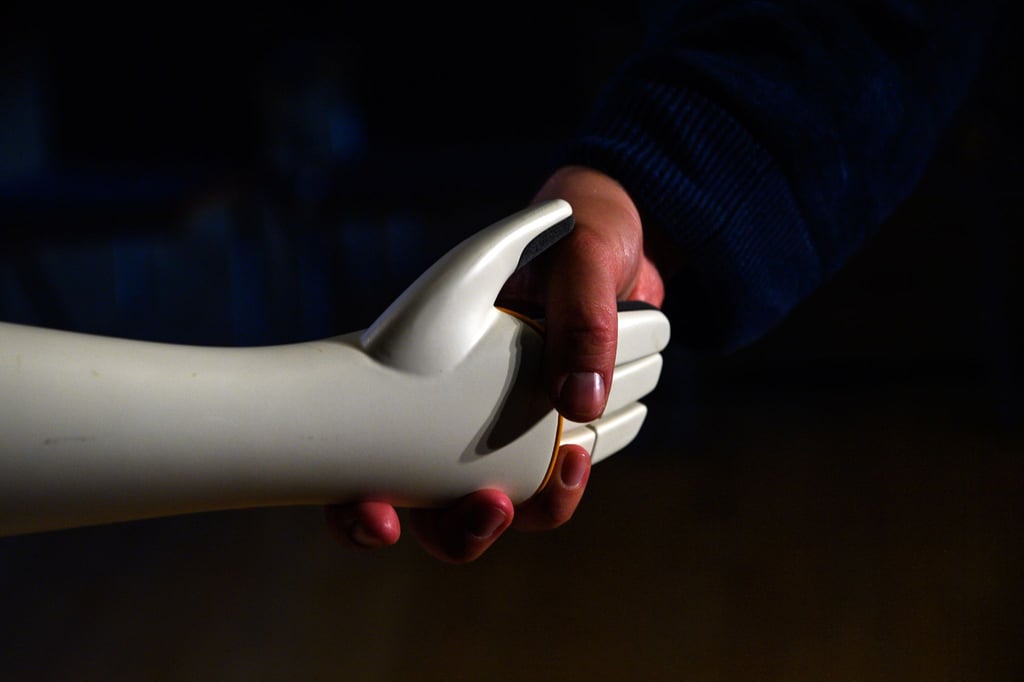 Eine menschliche Hand greift die Hand eines humanoiden Roboters.
