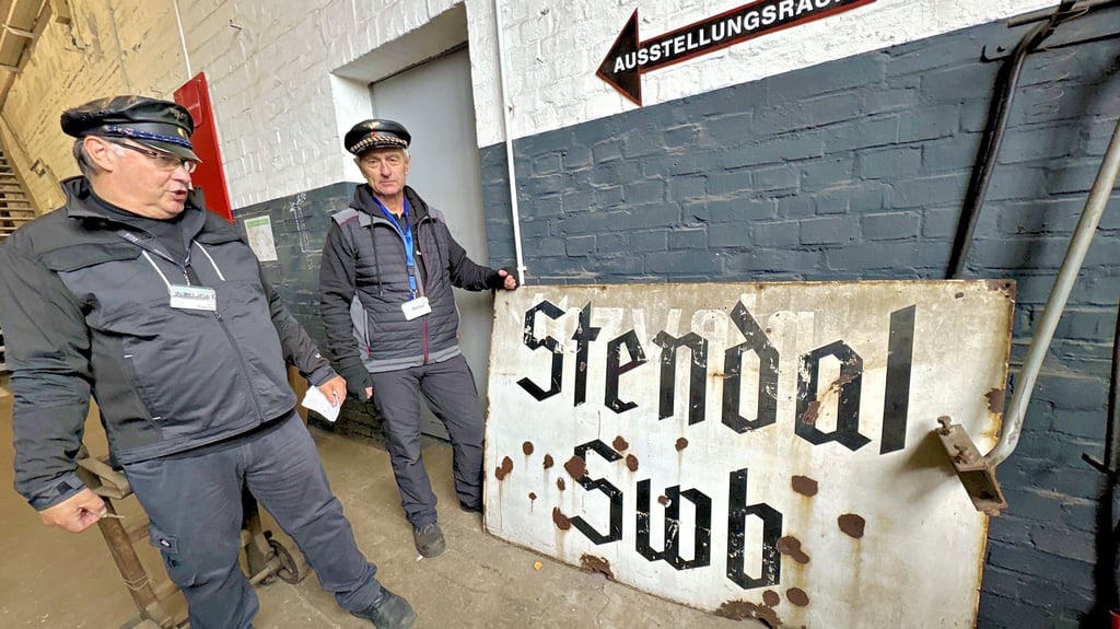 Bernd Klopsteg (links) und Peter Rohde vom Verein Dampflokfreunde Salzwedel im Museum Historischer Lokschuppen in Wittenberge an einem Schild des alten Bahnhofs Stendal Süd.