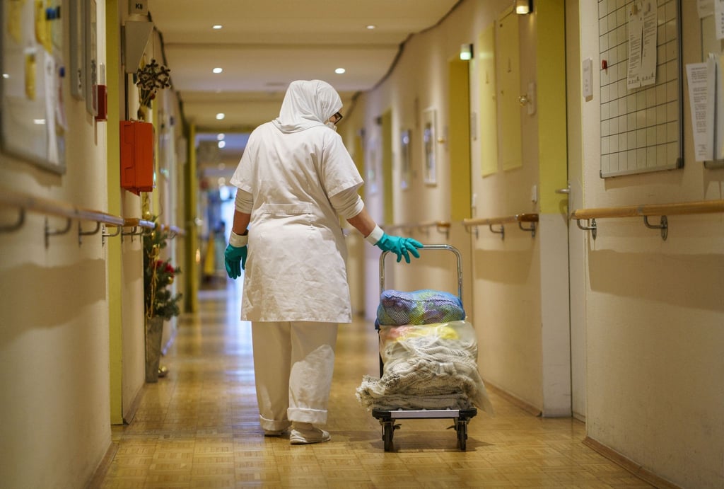 Eine Reinigungskraft zieht einen Wagen mit Wäsche durch einen Gang in einem Alten- und Pflegeheim.