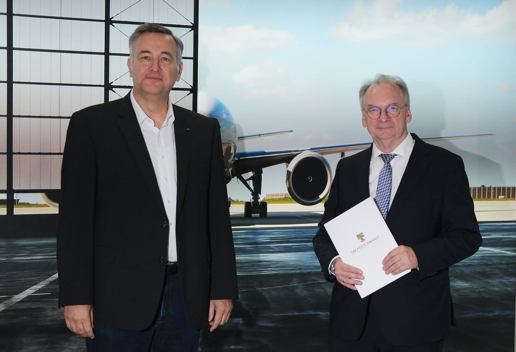 Markus Otto (l) und Reiner Haseloff (CDU) stehen im Flughafen Leipzig/Halle vor dem Plakat eines Flugzeugs.