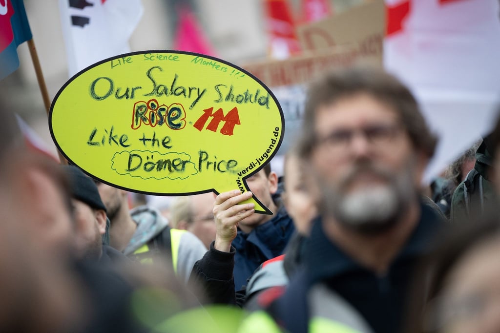 „Our Salary should rise like the Döner Price“ (dt. „Unser Gehalt soll so steigen wie der Dönerpreis“) steht auf einem Schild.