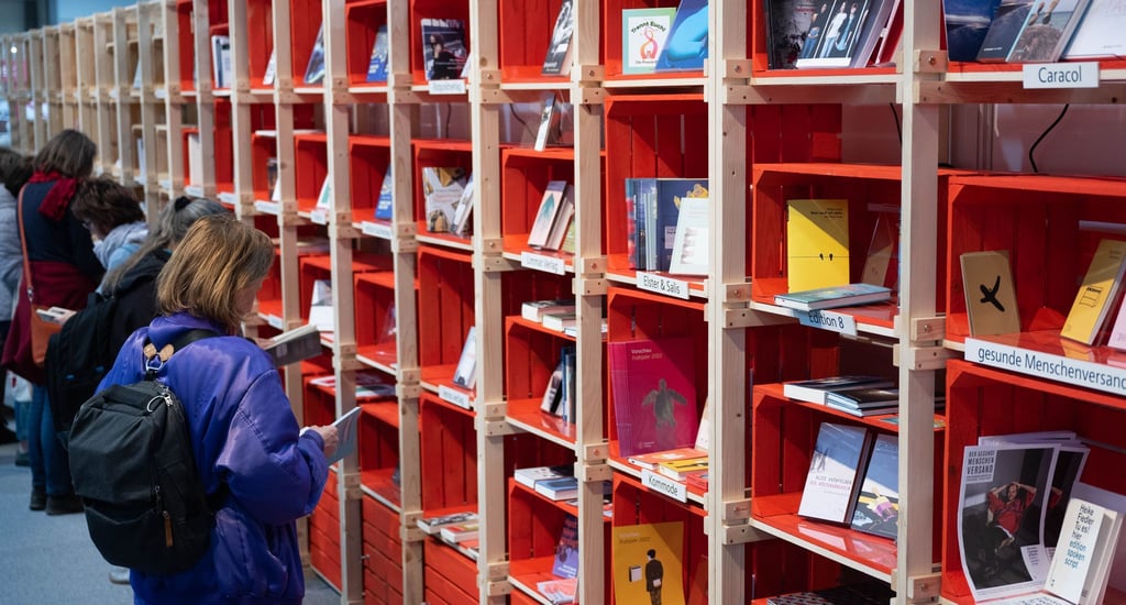 Besucherinnen und Besucher der Leipziger Buchmesse blättern in Büchern an einem Stand.