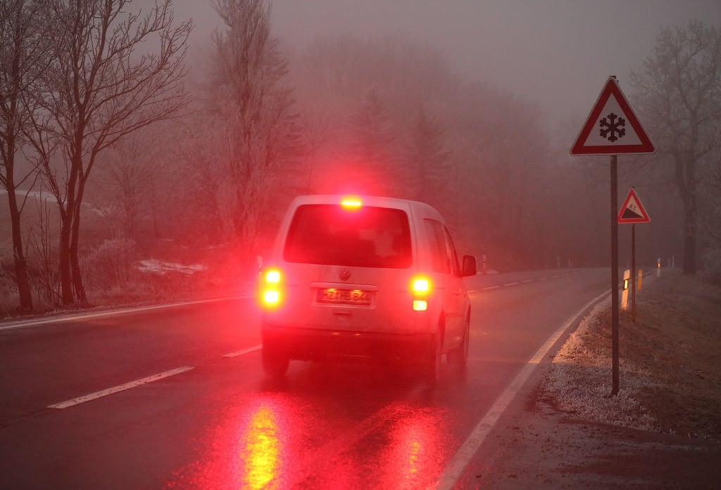 Ein Auto bremst an einem vernebelten Morgen auf einer Straße ab.