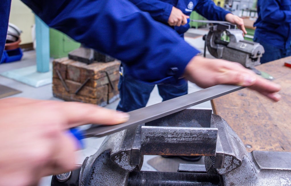 Lehrlinge arbeiten mit der Metallfeile an Schraubstöcken in einer Lehrwerkstatt.
