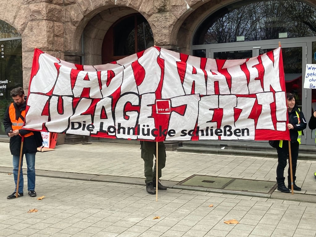 „Stadtstaaten - Zulage jetzt! - Die Lohnlücke schließen“ steht auf einem Plakat, das Demonstrierende vor dem Gewerkschaftshaus halten.