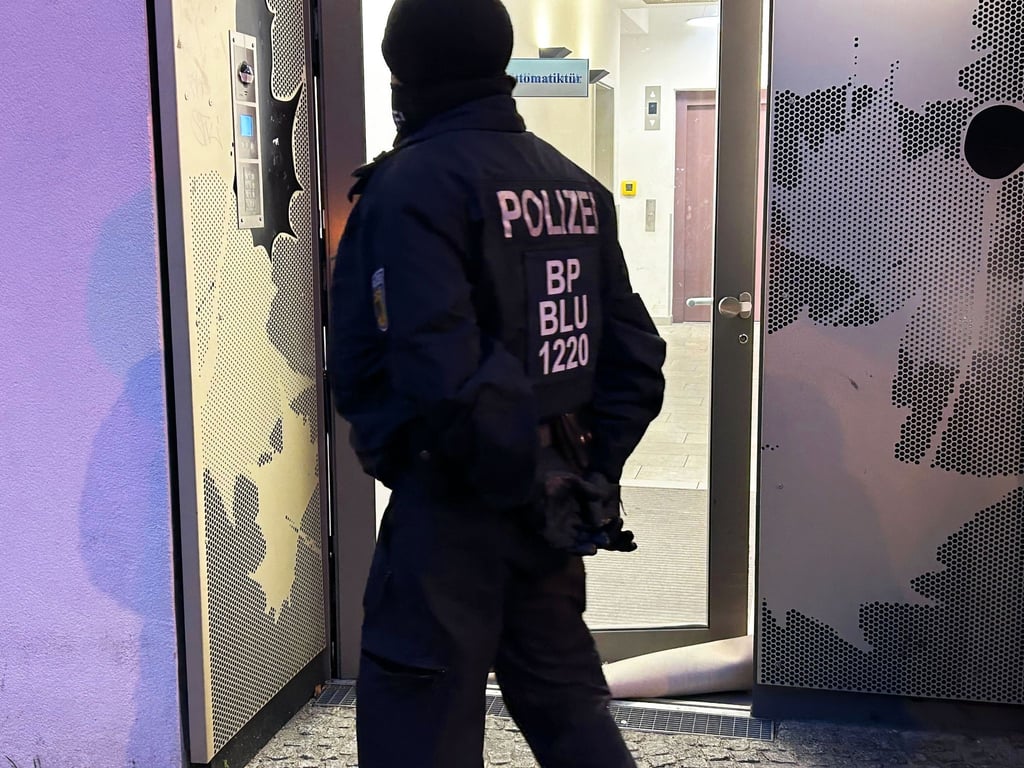 Ein Polizeibeamter steht bei einer Razzia in Berlin-Adlershof vor einem Gebäude.