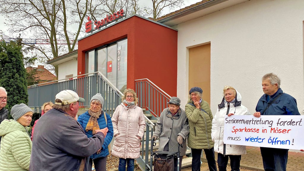 Der Seniorenbeirat Möser hat zu einer Demonstration vor der Sparkassen-Filiale in Thälmannstraiße aufgerufen – rund 20 Senioren sind gekommen, um ihren Unmut kundzutun. Die Filiale ist seit Sommer 2022 wegen der Sprengung von Geldautomaten gesperrt.
