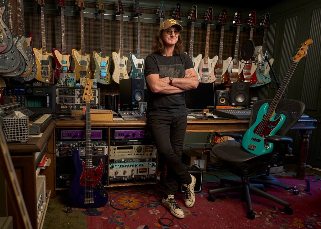 Der Rush-Frontmann Geddy Lee steht in seinem Studio, Bassgitarren hängen an der Wand.
