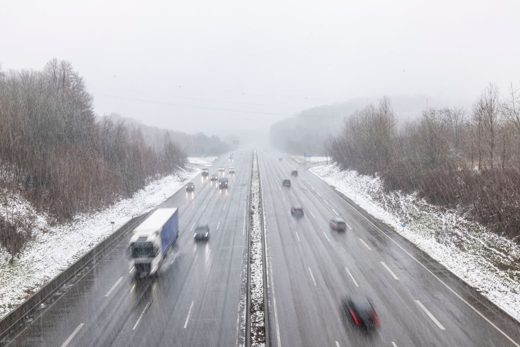 Autos fahren im Schneefall auf einer Autobahn.