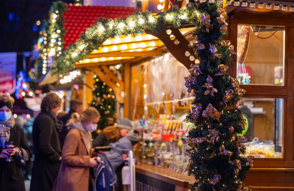 Besucher eines Weihnachtsmarktes stehen an einem Verkaufsstand für Süßigkeiten.