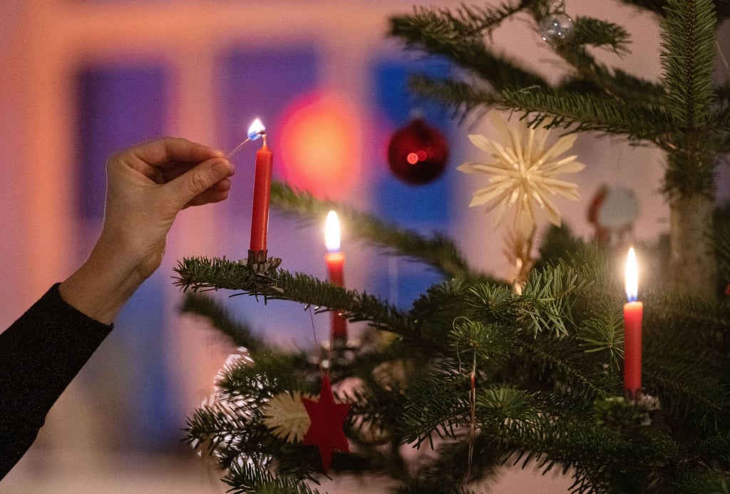 Eine Frau zündet eine Kerze an einem Weihnachtsbaum an.