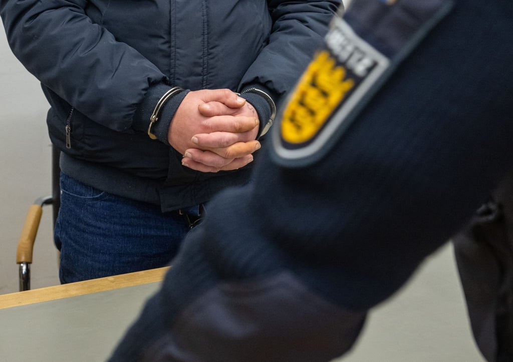 Der angeklagte 41-Jährige steht mit Handschellen im Landgericht. Er gab zu, im Frühjahr 2023 auf einem Schulhof seine siebenjährige Tochter ermordet zu haben.