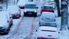 Schnee liegt am frühen Morgen auf Autos in der Hauptstadt, während ein Kleintransporter über eine glatte Straße mit Kopfsteinpflaster fährt.
