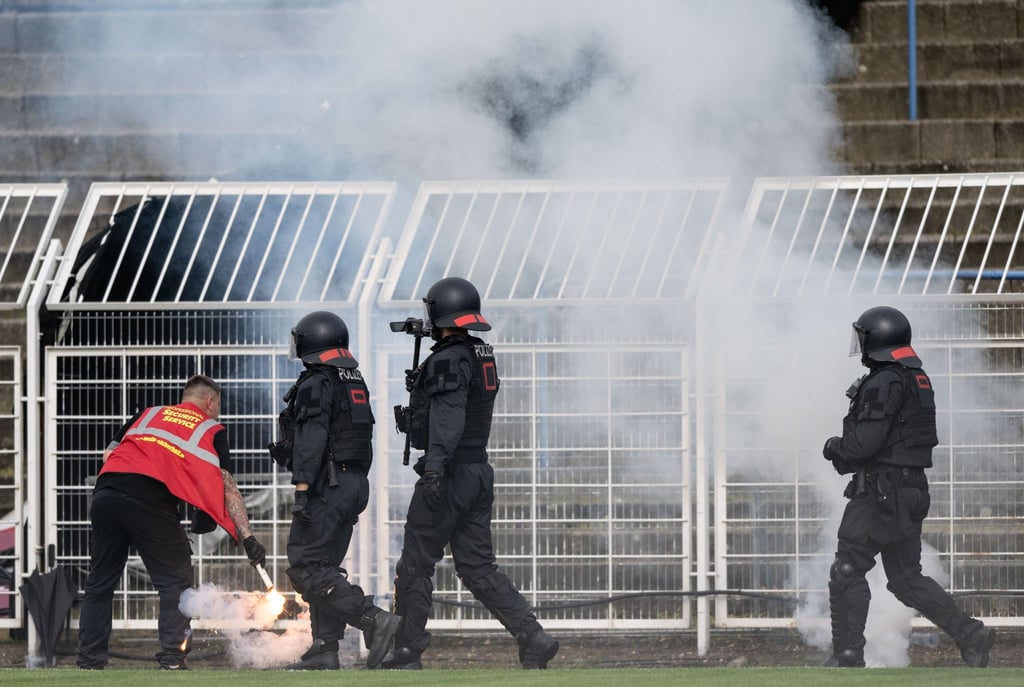 Ein Sicherheitsmitarbeiter löscht Pyrotechnik neben Polizisten im Bruno Plache Stadion.