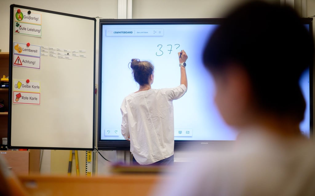 Eine Lehrerin schreibt eine Mathematikaufgabe auf eine digitale Schultafel im Klassenraum.