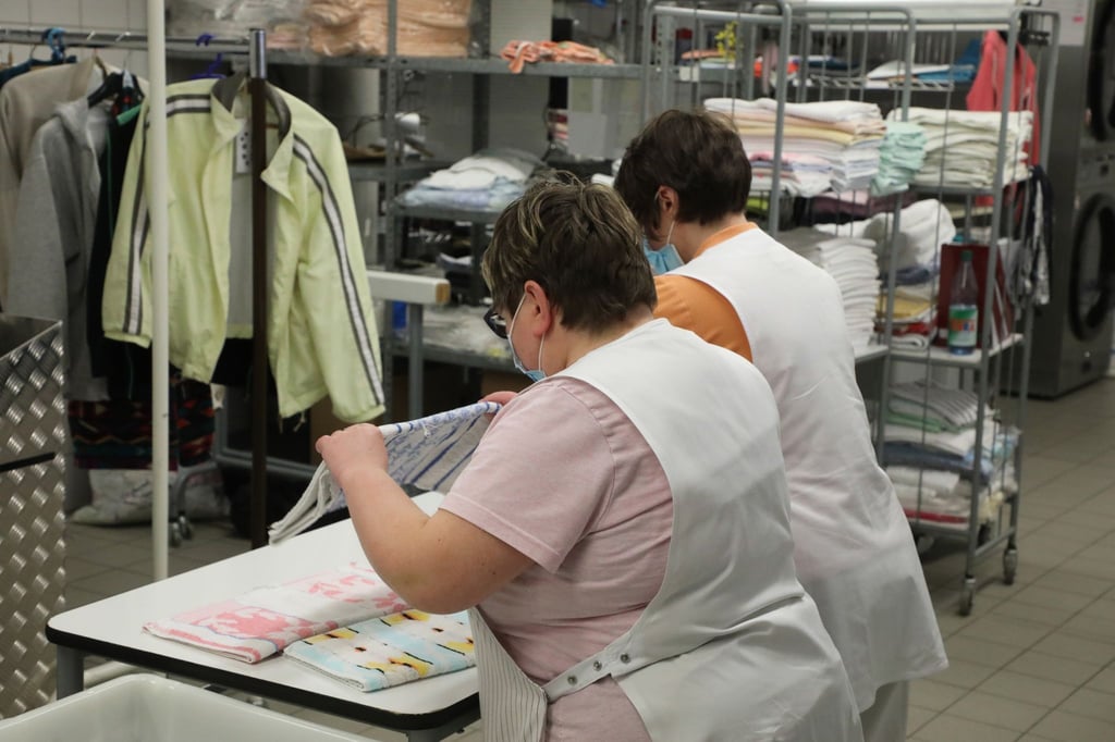 Zwei Frauen arbeiten in der Wäscherei der Lebenshilfe Gera e.V und legen dort Wäsche zusammen.