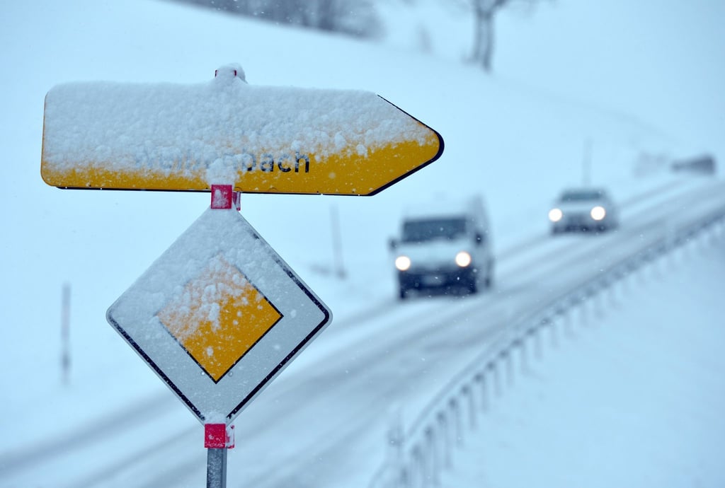 Neuschnee bedeckt ein Vorfahrtsschild und einen Wegweiser.