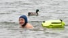 Comedian Wigald Boning schwimmt neben einer Ente in einem See.