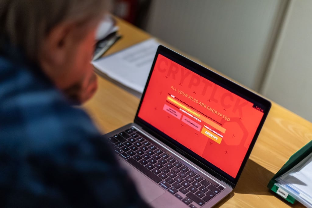 Ein Mann sitzt vor einem Laptop, der mit einem Verschlüsselungstrojaner (Ransomware) befallen ist.