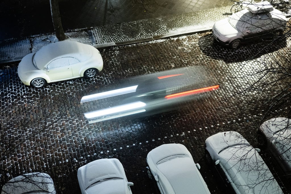 Ein Auto fährt an zugeschneiten parkenden Autos vorbei.