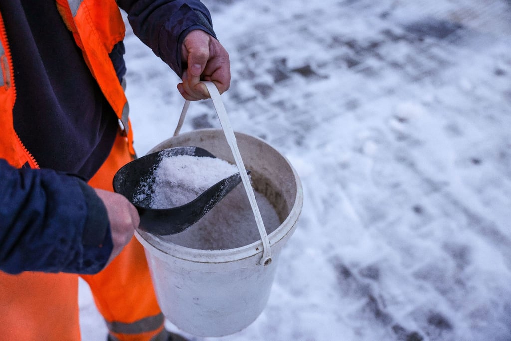 Ein Mitarbeiter des Winterdienstes verteilt Streusalz auf einem Fußweg.