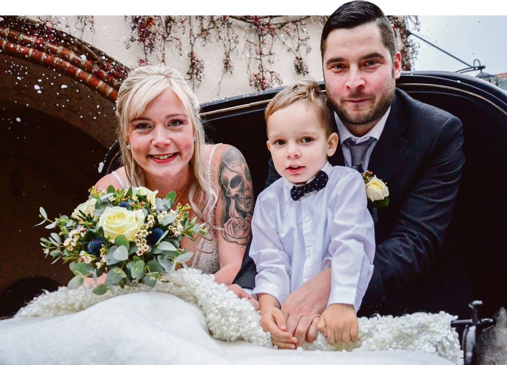 Vivien und Philip Hauf mit Söhnchen Leon (4) posieren nach ihrer Nikolaushochzeit vor winterlicher Kulisse samt Kutsche und Kunstschneeflocken.