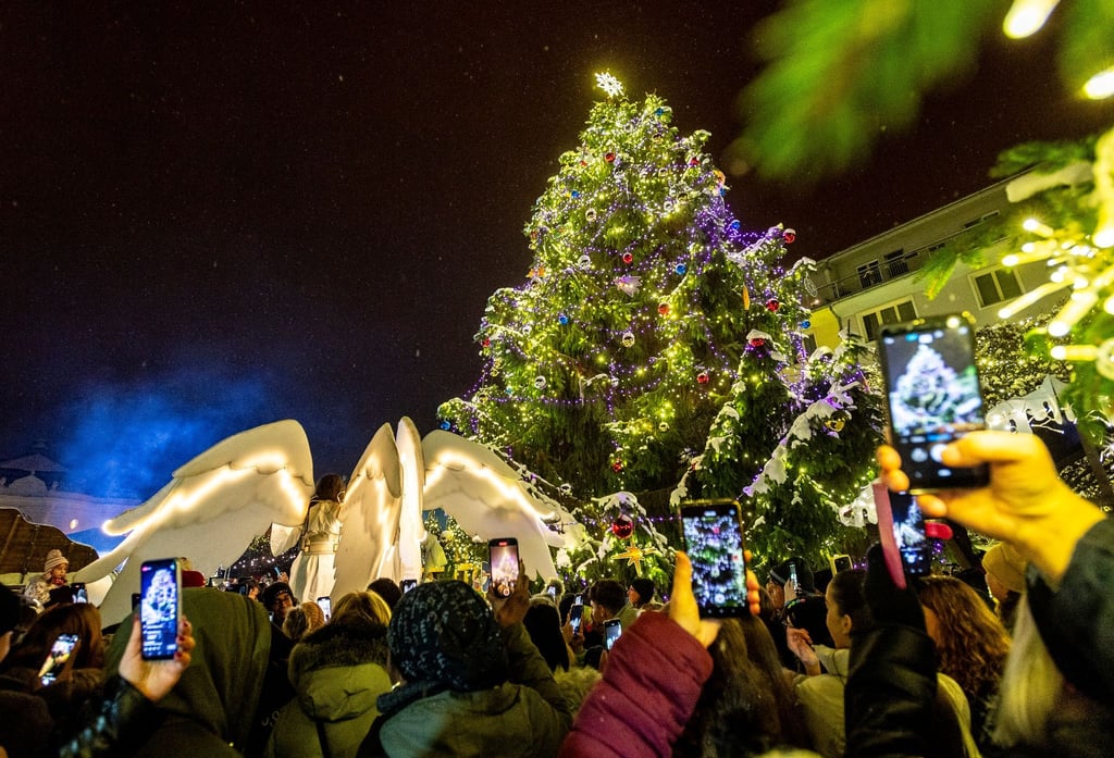Menschen sehen sich neben einem großen geschmückten Weihnachtsbaum eine Theater-Aufführung an.
