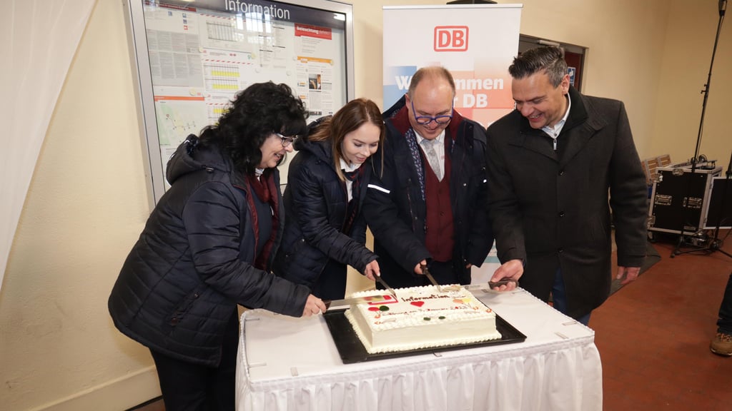 Mitarbeitende der Deutschen Bahn, darunter eine Auszubildende, schneiden eine Torte bei der Eröffnung des Juniorbahnhofs in Köthen an.