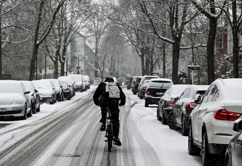 Ein Radfahrer fährt auf einer mit Schnee bedeckten Straße in Karlshorst, auf der die Spuren von Autos zu sehen sind.