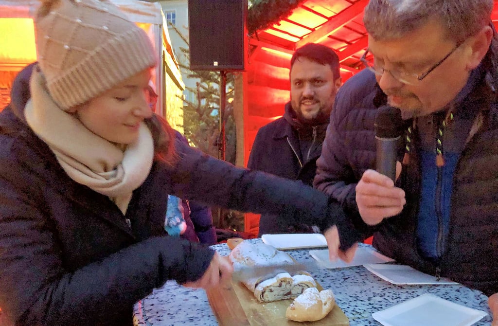 Stollen anschneiden auf dem Zeitzer Weihnachtsmarkt: Konditorin Magdalena Radefeld und Hajo Bartlau, Pressesprecher der Stadtwerke Zeitz, eines der Sponsoren des Weihnachtsmarktes, laden zum Kosten des Knusperstollens ein.