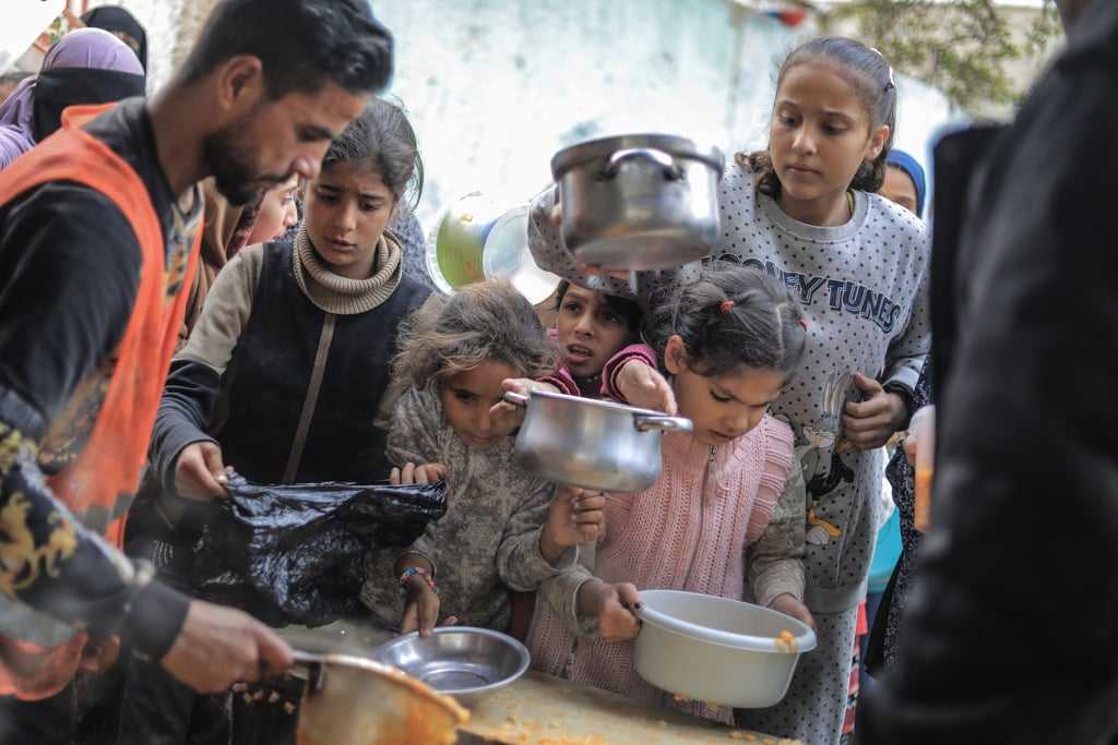 Menschen stehen in Rafah im Süden des Gazastreifens mit Töpfen, Schalen und Tüten bei einer Essensausgabe an.