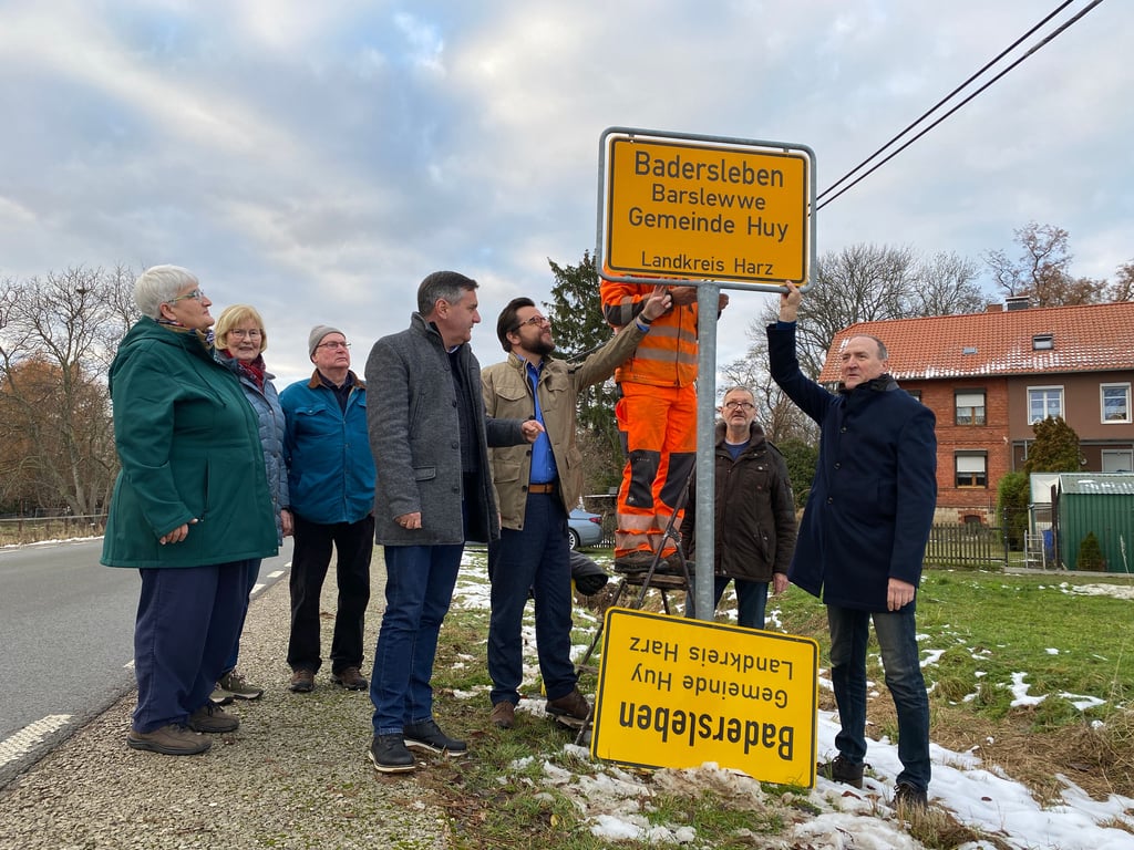Im Beisein von interessierten Baderslebern, Ortsbürgermeister Olaf Beder (re.), Huy-Bürgermeister Maik Berger (Vierter von rechts) und Landrat Thomas Balcerowski (Vierter von links) wurde das neue Schild in Badersleben aufgebaut.
