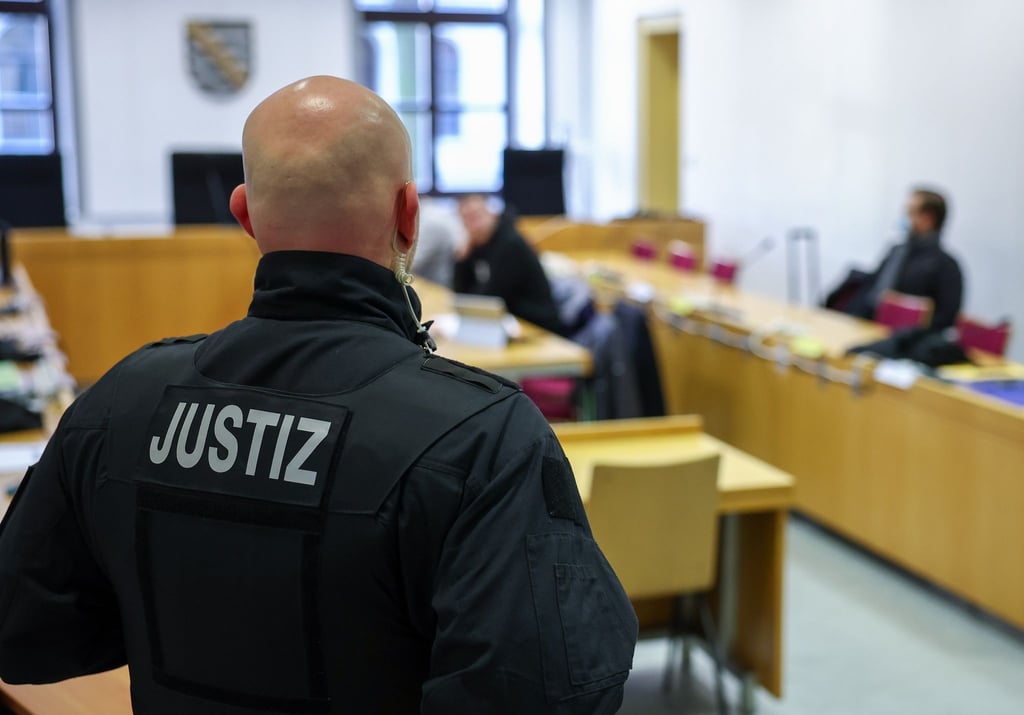 Ein Justizbeamter steht vor Prozessbeginn vor einigen Angeklagten im Landgericht Chemnitz.