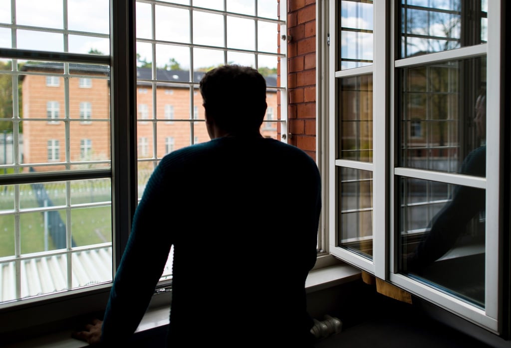 Ein Straftäter steht vor einem vergitterten Fenster in einer Klinik für Forensische Psychiatrie.