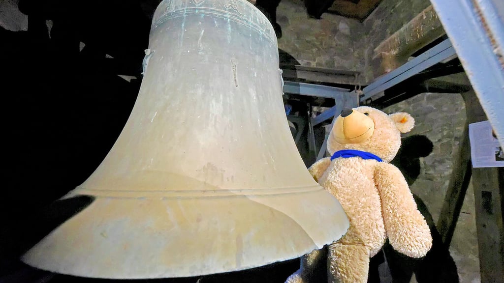 Der Teddy sieht sich die Bronzeglocke an, deren Riss geschweißt werden muss. Spenden werden gesammelt.