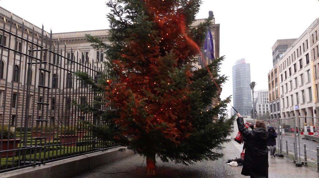 Ein Mitglied der Klimaschutzgruppe besprüht einen Weihnachtsbaum vor dem Bundesrat mit orangener Farbe.