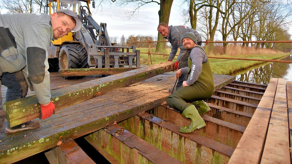 Stefan Schmidt (v.l.), Marko Bröckel und Angelo Buchwald von der Zimmerei und Dachdeckerei „Pro Dach 23“ ersetzen die maroden Balken der Brücke auf dem Sachauer Damm bei Mannhausen durch neue Eichenbohlen.