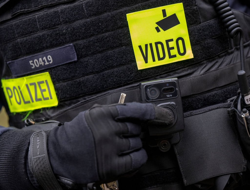 Ein Polizist schaltet bei einem Pressetermin die Bodycam auf seiner Uniform ein.