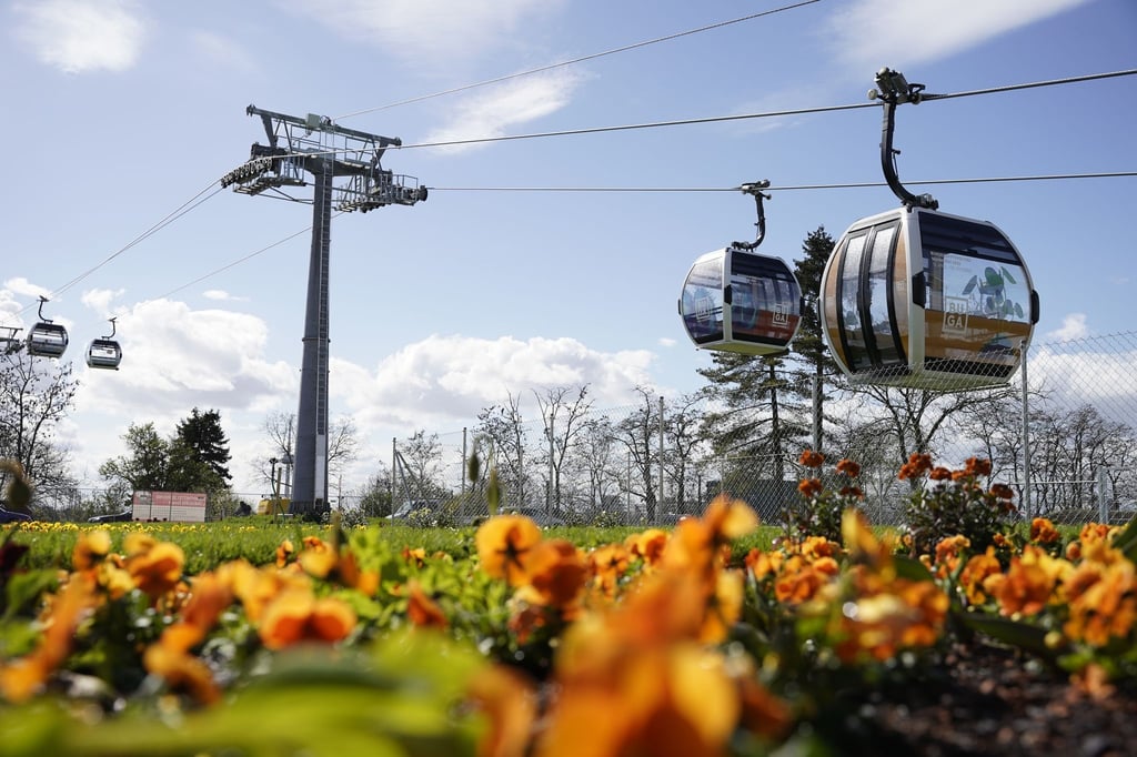 Kabinen der Seilbahn fahren auf dem Gelände der Bundesgartenschau 2023 in Mannheim hinter einem Blumenbeet.