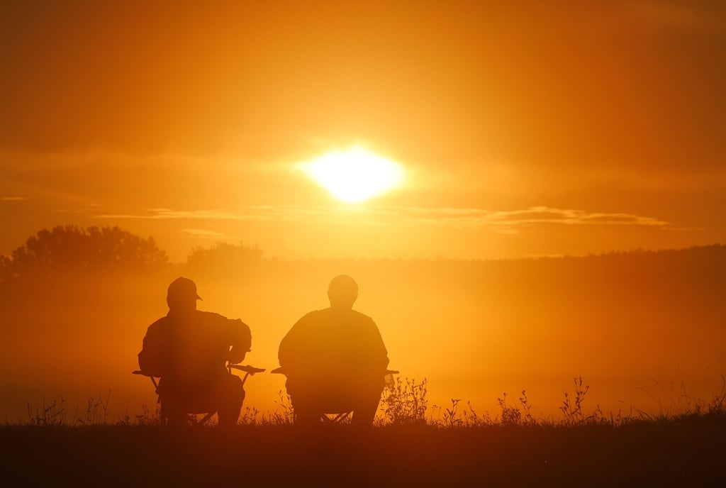 Zwei Angler sitzen auf Campingstühlen und schauen sich den Sonnenaufgang an.